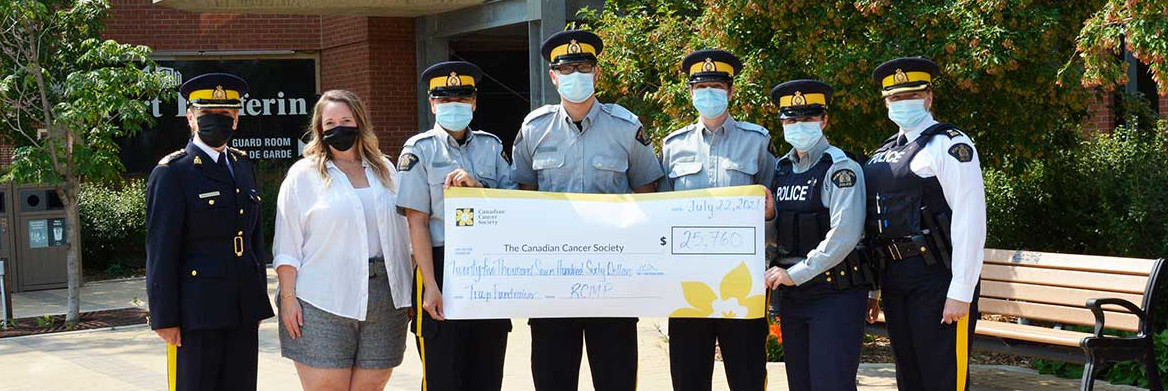 Six uniformed RCMP officers and one civilian female stand in a row holding a giant check.