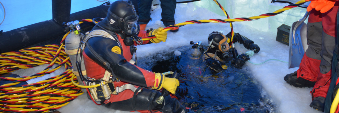 People wearing dive gear swimming in icy waters surrounded by equipment.