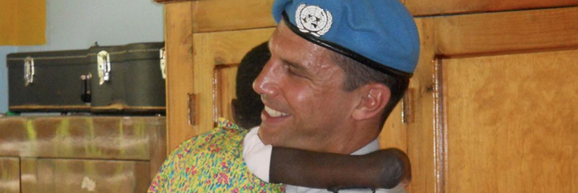 Young Haitian girl hugs smiling RCMP officer as he holds her in his arms.