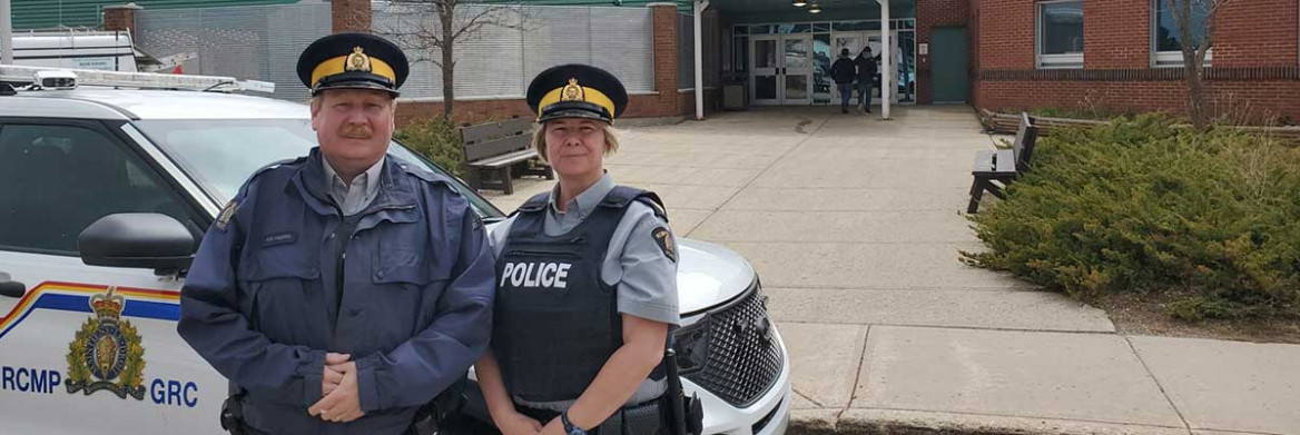 Deux policiers de la GRC devant une autopatrouille garée près d'une école.