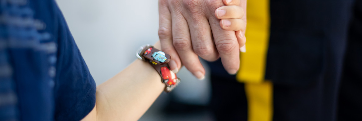 A female RCMP officer holds the hand of a young child, in front of a house.