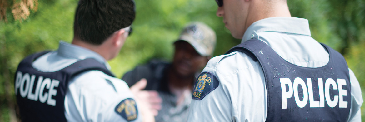 Two police officers speak to a man in dense forest.