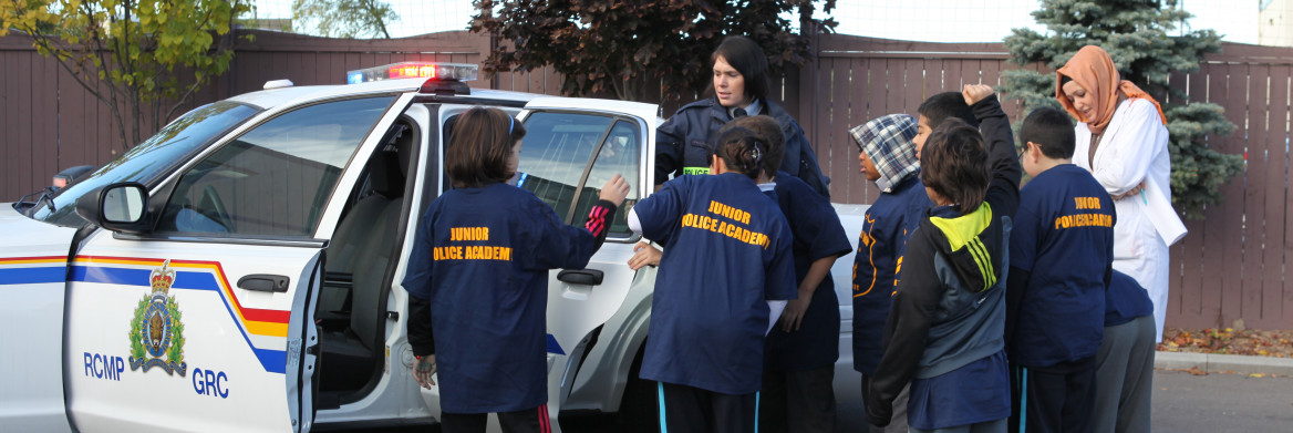 Group of school children and two women looking at police cruiser.