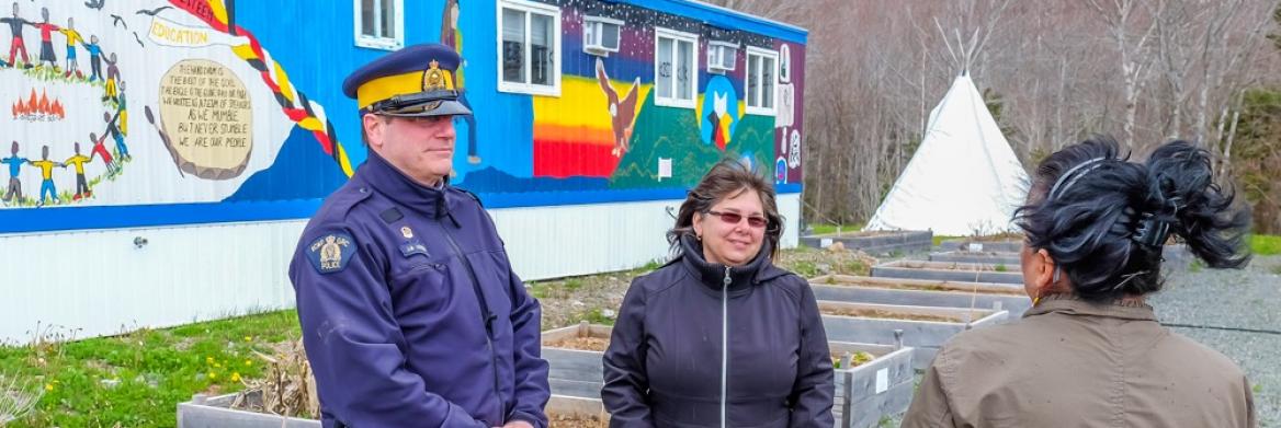 A male police officer and two women stand in front of a building bearing a colourful mural.