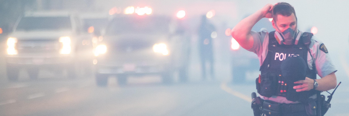 Male police officer wearing mask on a street surrounded by smoke.