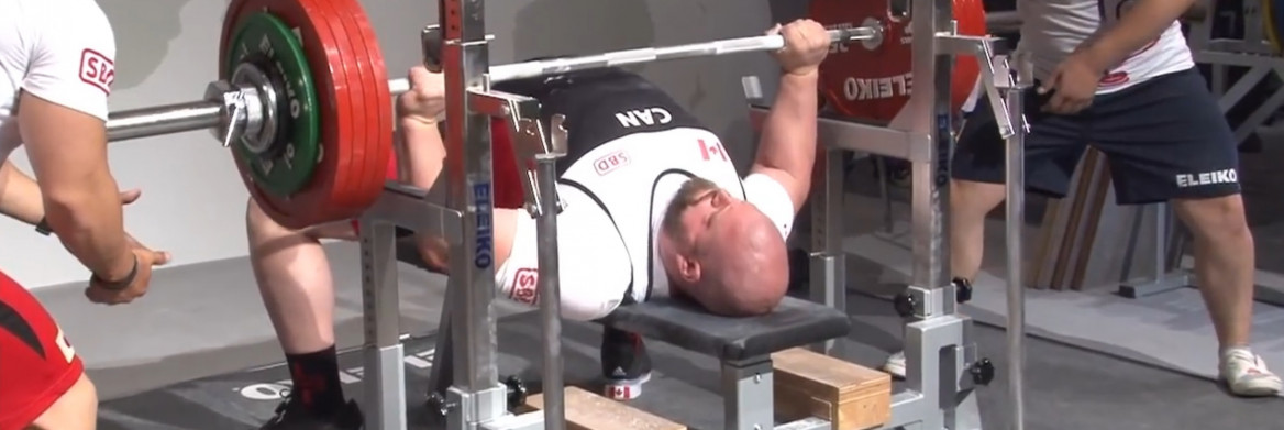 A man lays on a weight bench, holding a bar with large weights on each end. 