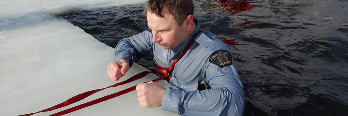 Un agent de la GRC se tient dans l'eau glacée avec une corde de sécurité attachée autour de la poitrine.