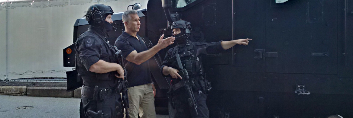 Homme debout avec deux hommes vêtus d'équipement policier noir.