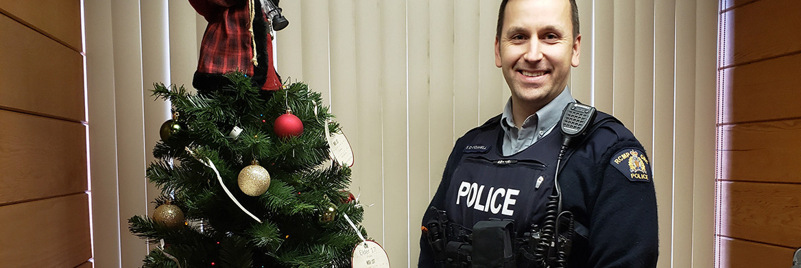 An RCMP officer stands beside a decorated Christmas tree. 