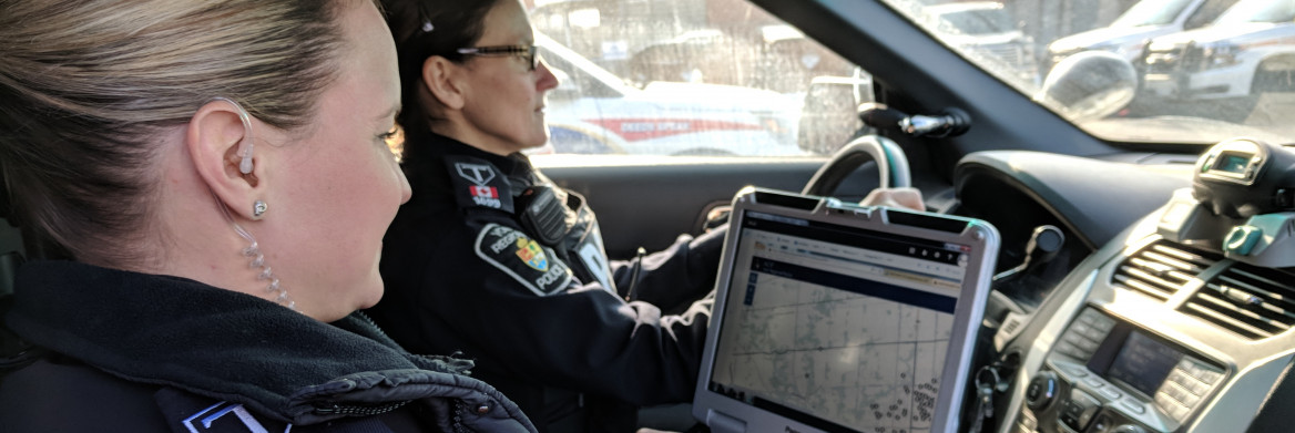 Two female police officers looking at a computer screen in a cruiser.