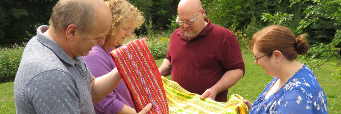 Two men and two women examine a red shawl and a yellow shawl.