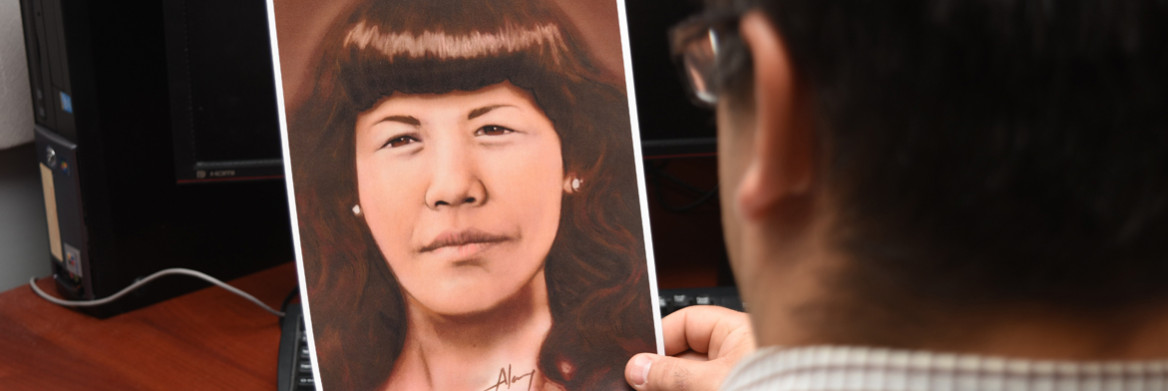 Homme assis à un bureau tenant dans ses mains le portrait d'une femme. 