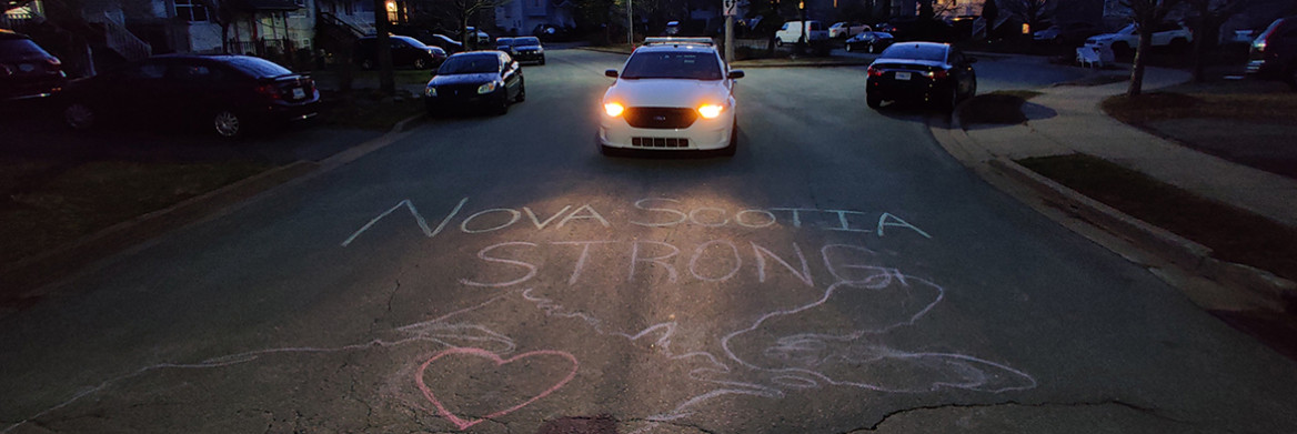 Une autopatrouille stationnée dans une rue résidentielle au crépuscule. Les mots Nova Scotia Strong sont tracés à la craie sur l'asphalte.