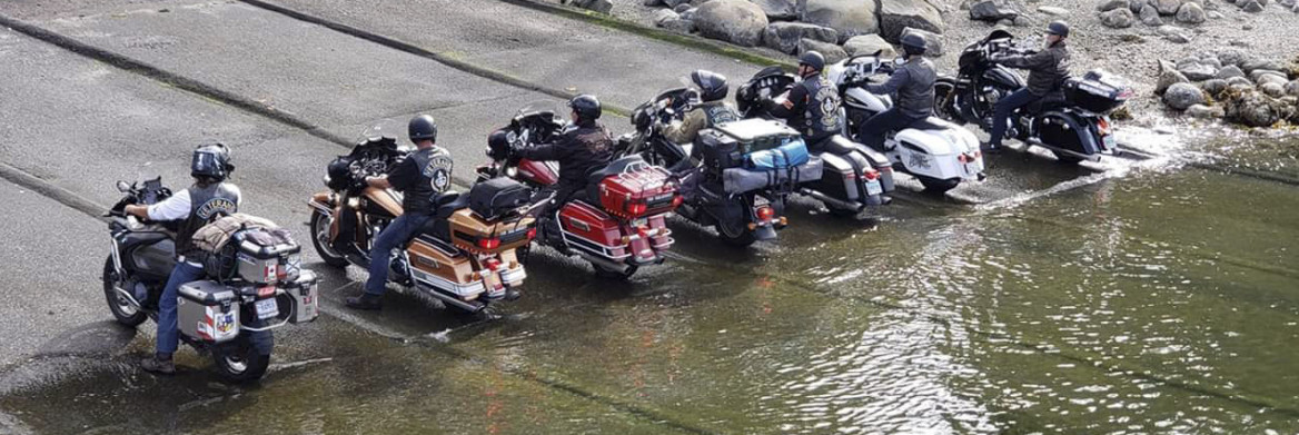 Des motocyclistes sont assis sur leurs motos, dont les pneus arrière touchent l'eau.