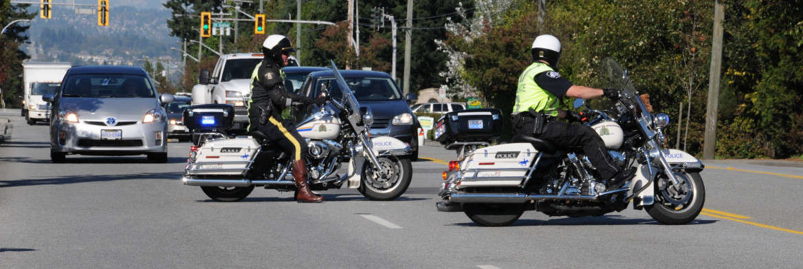 Two male police officers riding motorcycles in traffic. 