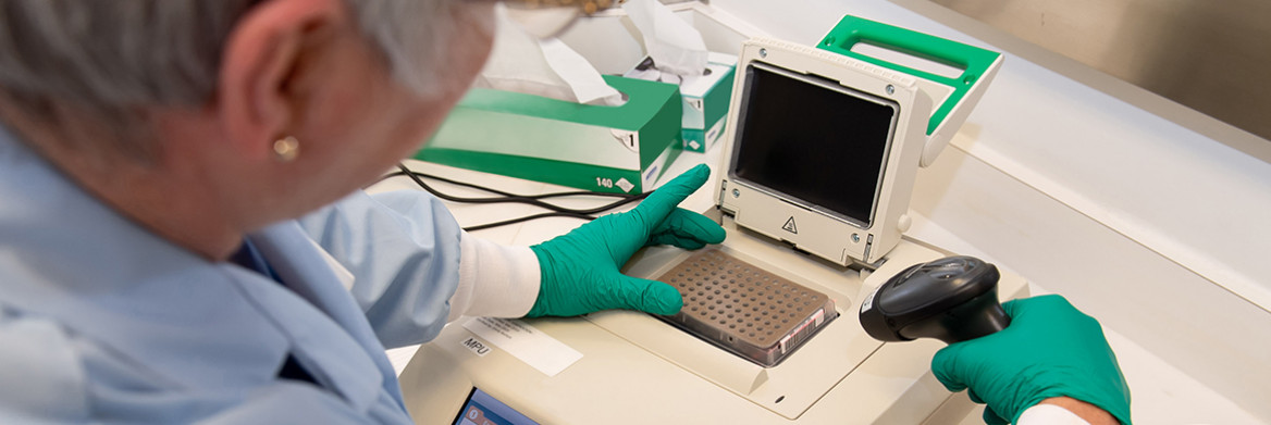 A woman working in a lab wearing a lab coat and gloves.