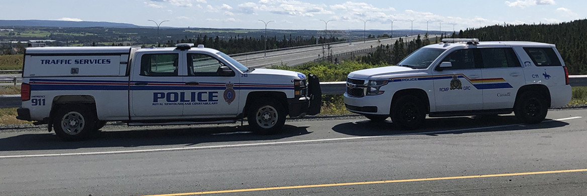 An RCMP vehicle and Royal Newfoundland Constabulary vehicle park beside reach other along a road. 