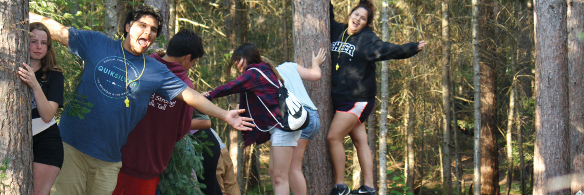 Kids stand on tight rope strung between trees in forest