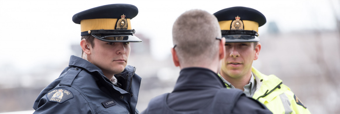 Two male officers listen to another officer while standing outdoors in winter.