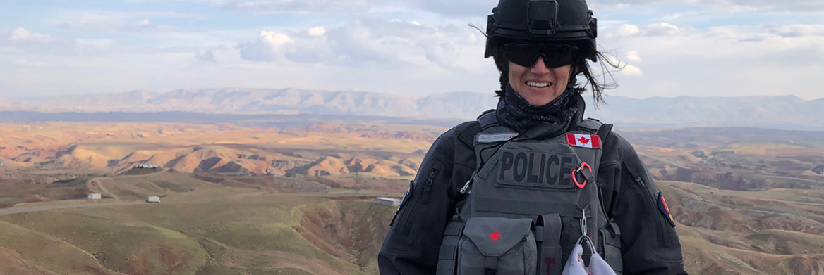 A female RCMP officer stands outdoors with a mountain range in the background.