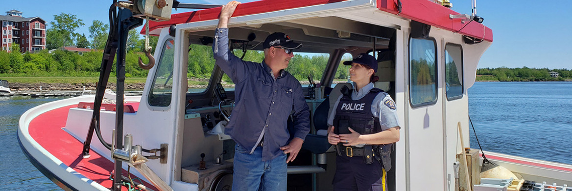 A female RCMP officer stands on a fishing boat with a man.