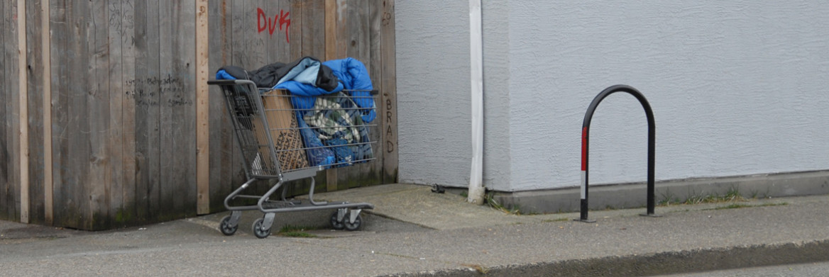 Un caddie rempli d'articles se tient seul sur le trottoir. Une clôture avec des grafitti est en arrière-plan.