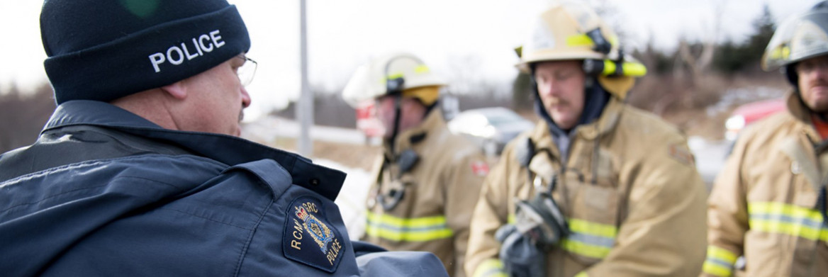 An RCMP officer in a winter cap talks to three firefighters.