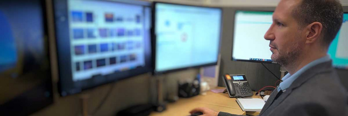 Un agent de la GRC en tenue de bureau est assis à un poste de travail devant plusieurs écrans d'ordinateur.