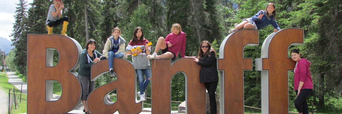 Seven Indigenous girls and one woman pose playfully outside on giant letters B-A-N-F-F.