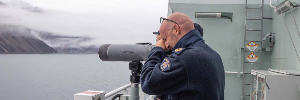 An RCMP officer looks through a telescope, secured on a ship's railing.