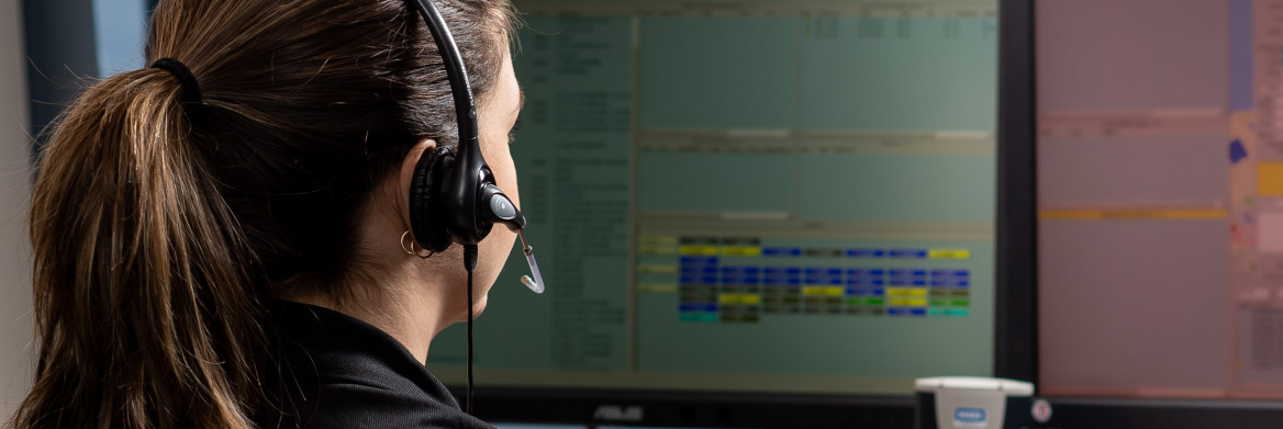 Une femme est assise à un ordinateur et parle en portant un casque d'écoute. 