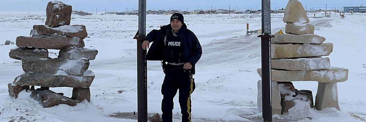 Male RCMP officer standing outdoors in a small community surrounded by snow.