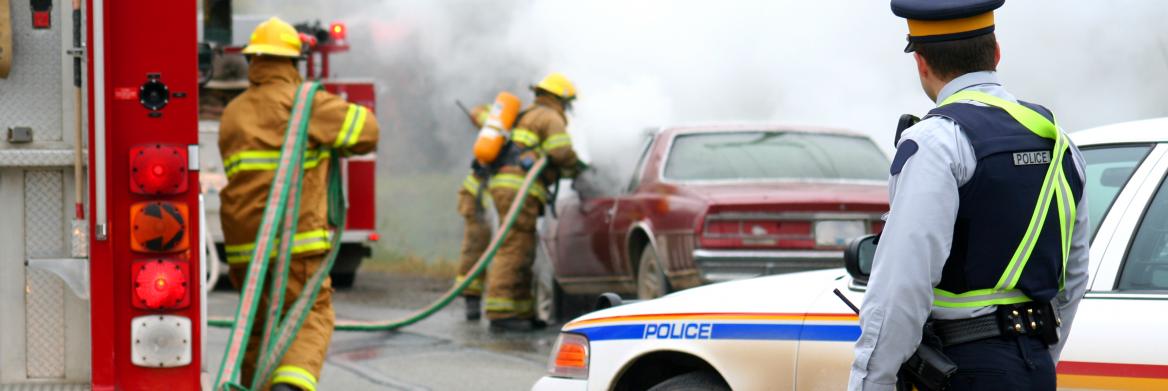 Des policiers et des pompiers autour d'un véhicule en flammes.