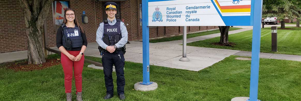 Un policier de la GRC en uniforme et une infirmière portant un gilet de protection muni de la mention « R-PACT » (l'équivalent anglais d'EPRIC) sur la poitrine devant un détachement de la GRC.