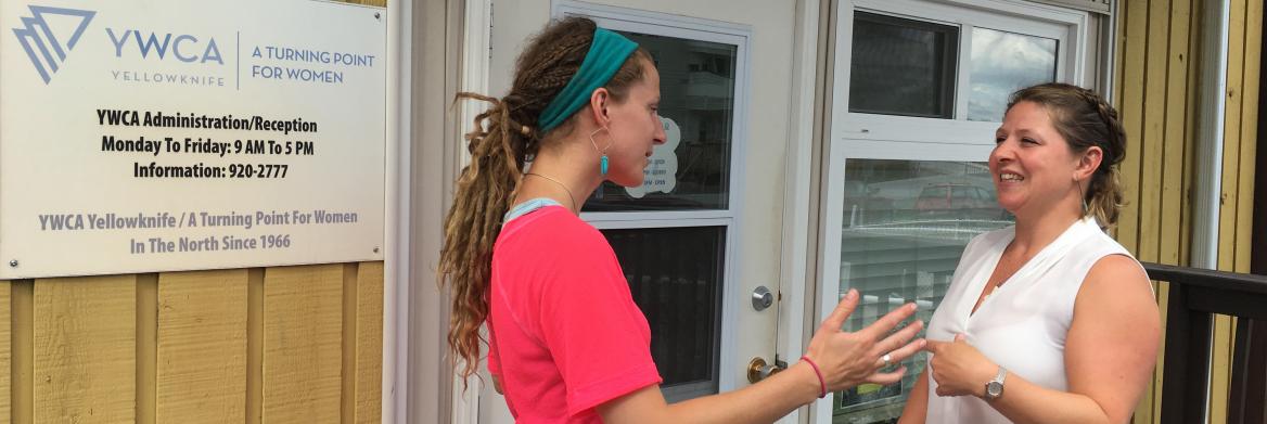 Two women talk in front of building.