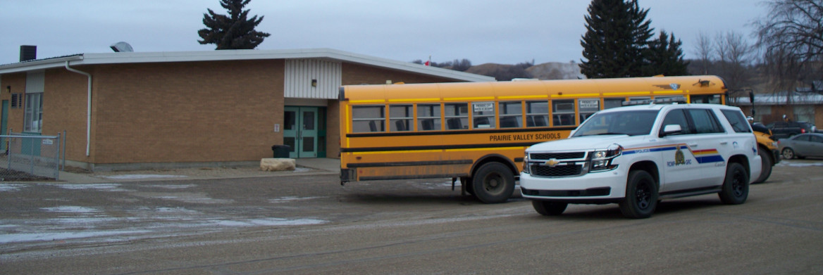 A yellow school bus is parked next to an RCMP vehicle outside of a school. 