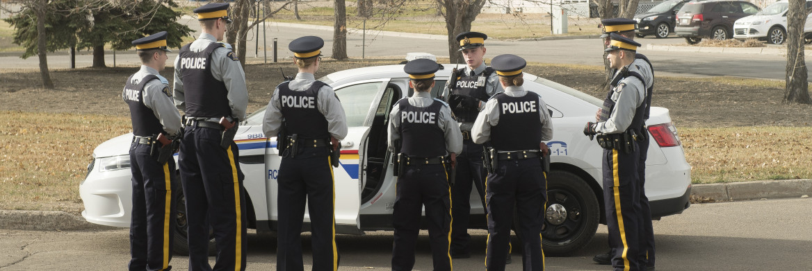 Groupe de cadets en uniforme debout en demi cercle autour d'un véhicule de police.