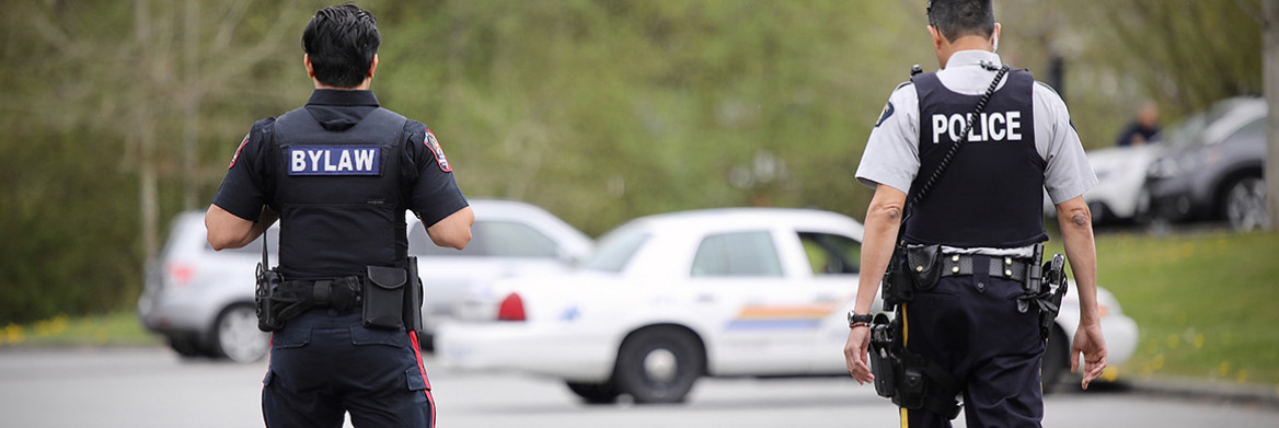 Two male officers walk side by side toward a parked police cruiser.