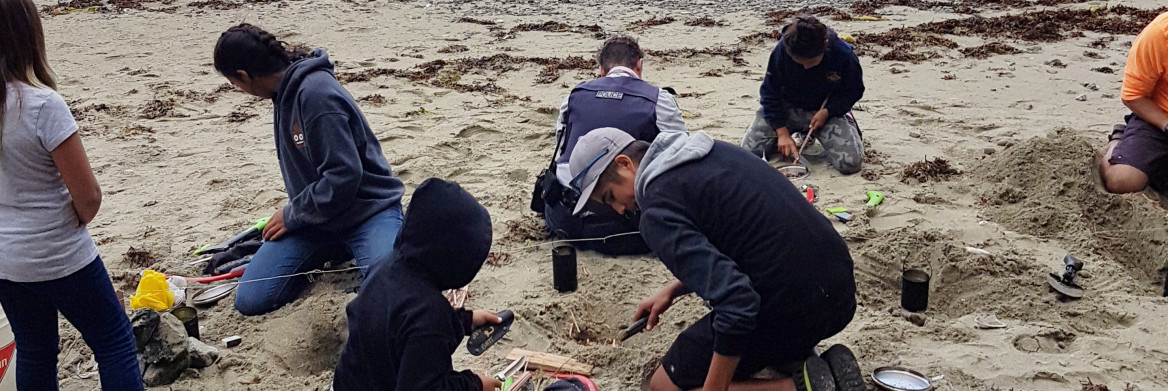 Un groupe de jeunes sur une plage placent des roches et des petites branches pour allumer des feux.