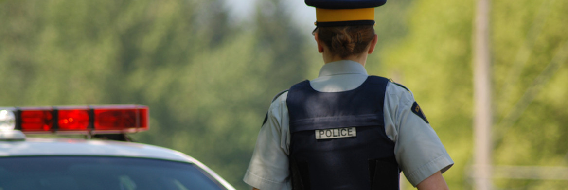 Vue arrière d'une femme agent de la GRC marchant à côté d'une voiture de police.