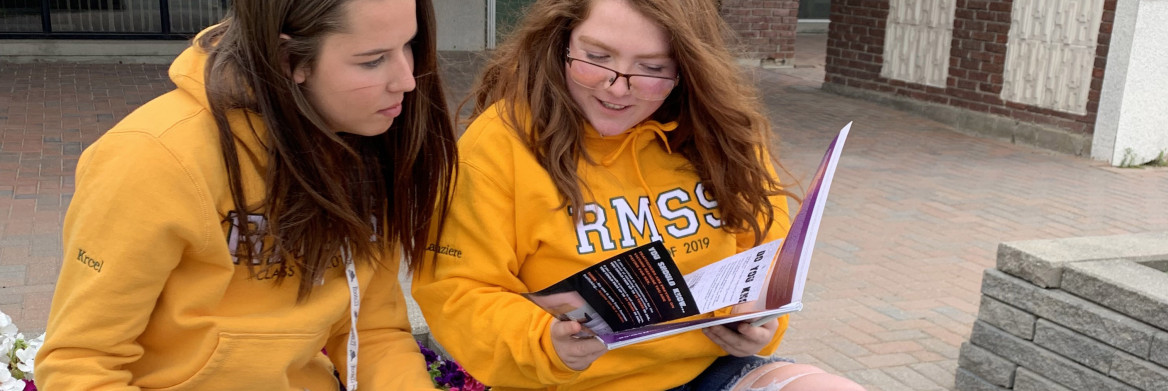 Two young women examine pamphlets while sitting on a bench.