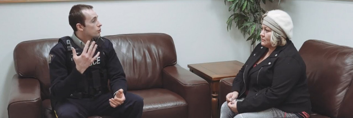 Male police officer sits on couch talking to female.