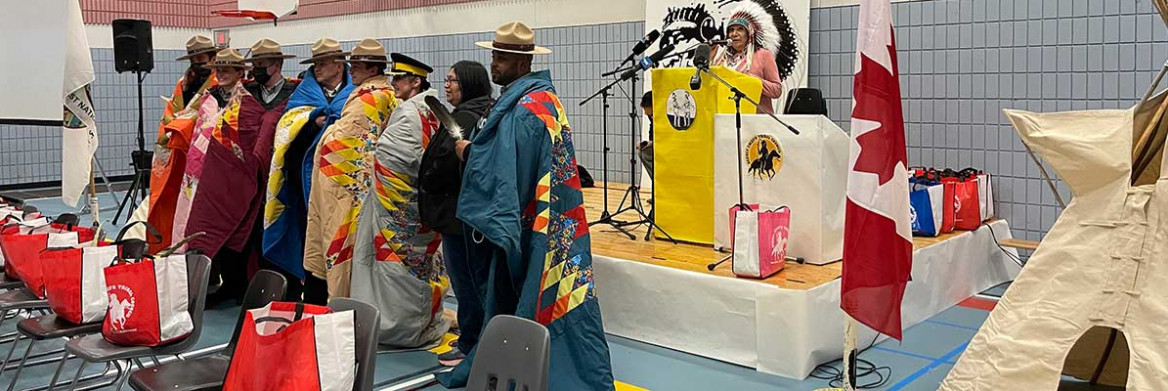 A group of RCMP officers, each wrapped in a colorful blanket, stand together with an Indigenous person.