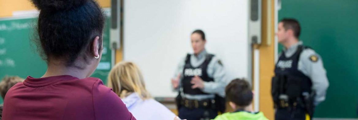 Two RCMP officers stand in front of a classroom full of students.