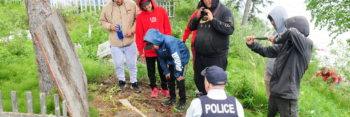 Un groupe de jeunes et un agent de la GRC regardent une parcelle de terre sur le sol.