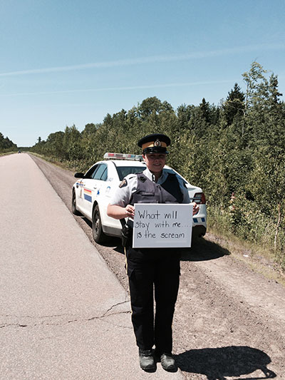 Cst. DeMerchant standing outside a police vehicle on side of highway, holding whiteboard: “What will stay with me…..is the scream”